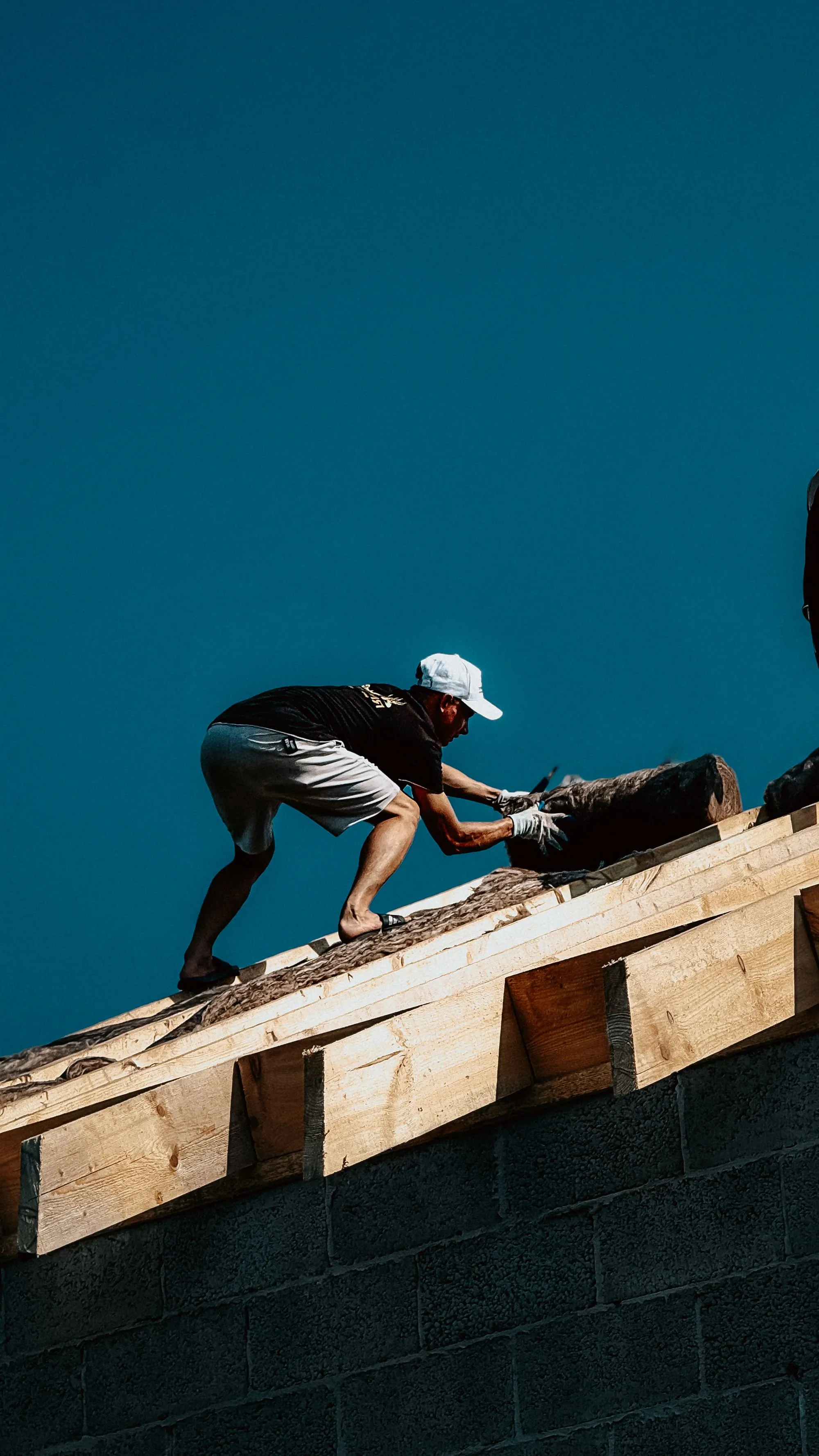 A roofer working along a bare roof edge against a clear sky