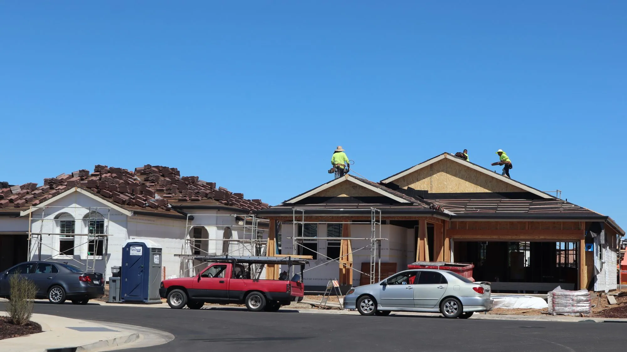 A newly framed suburban house with roofers at work on the slope above