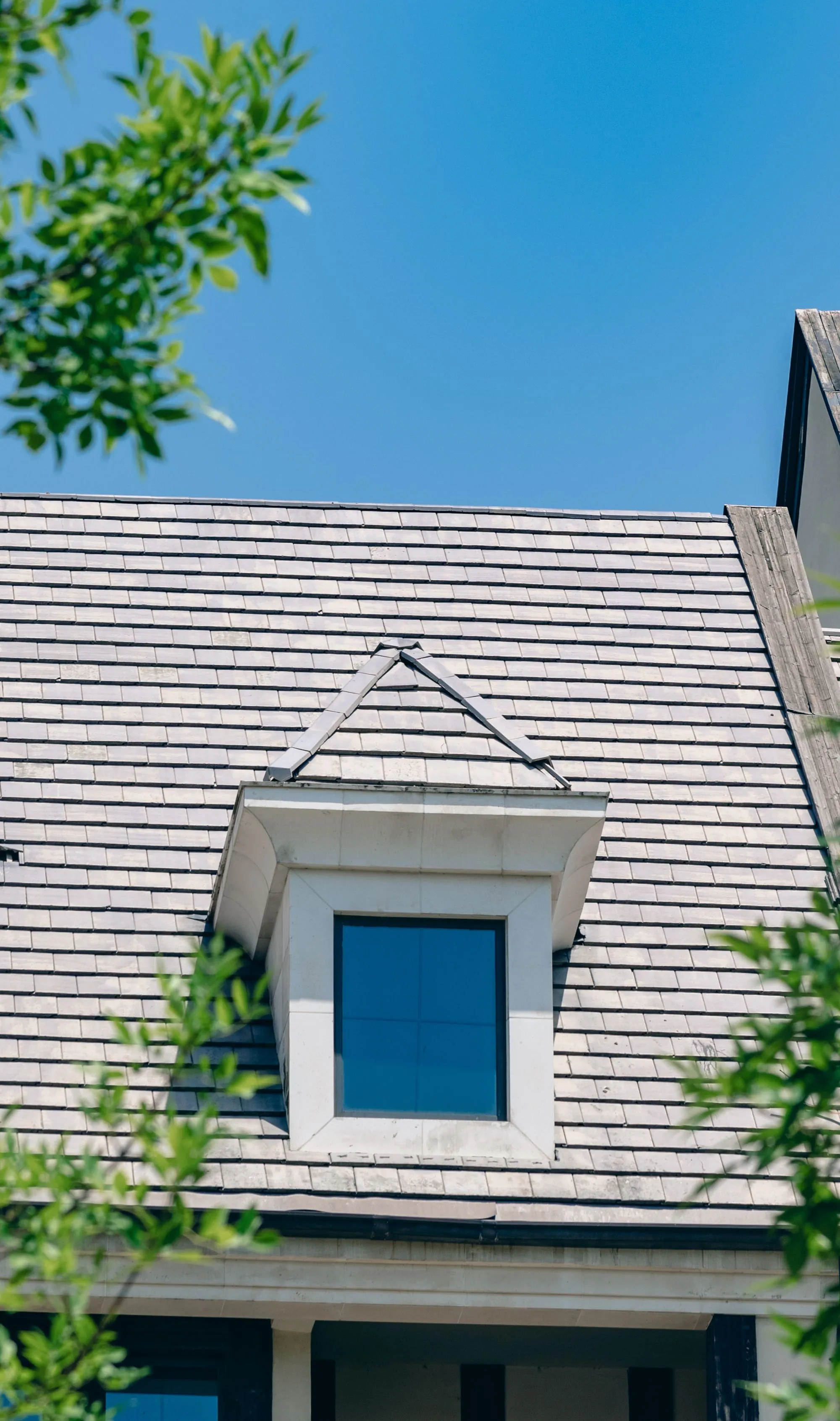 A shingled roof rising to a dormer against a pale sky
