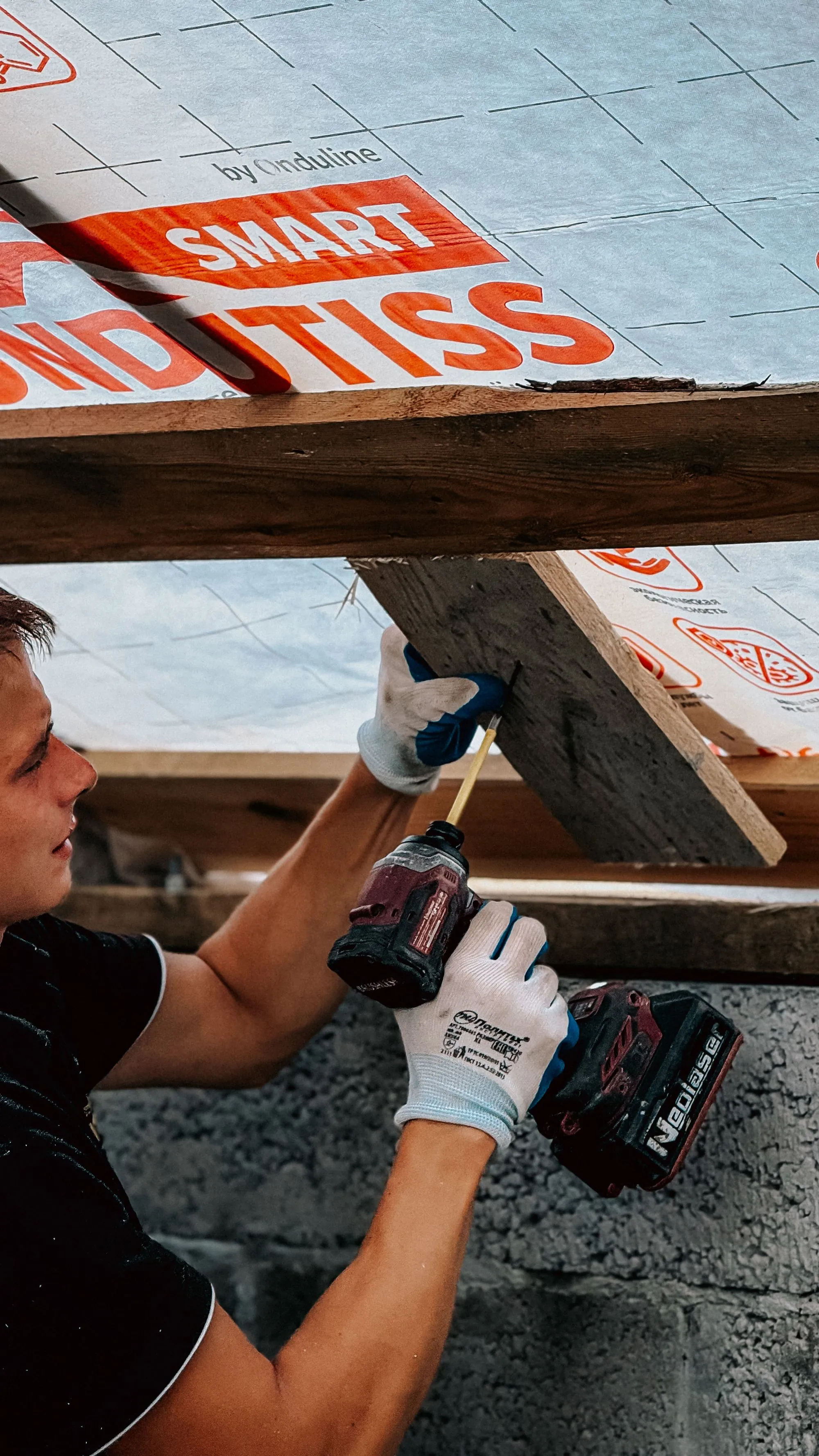 A worker fixing sheathing overhead with a cordless drill