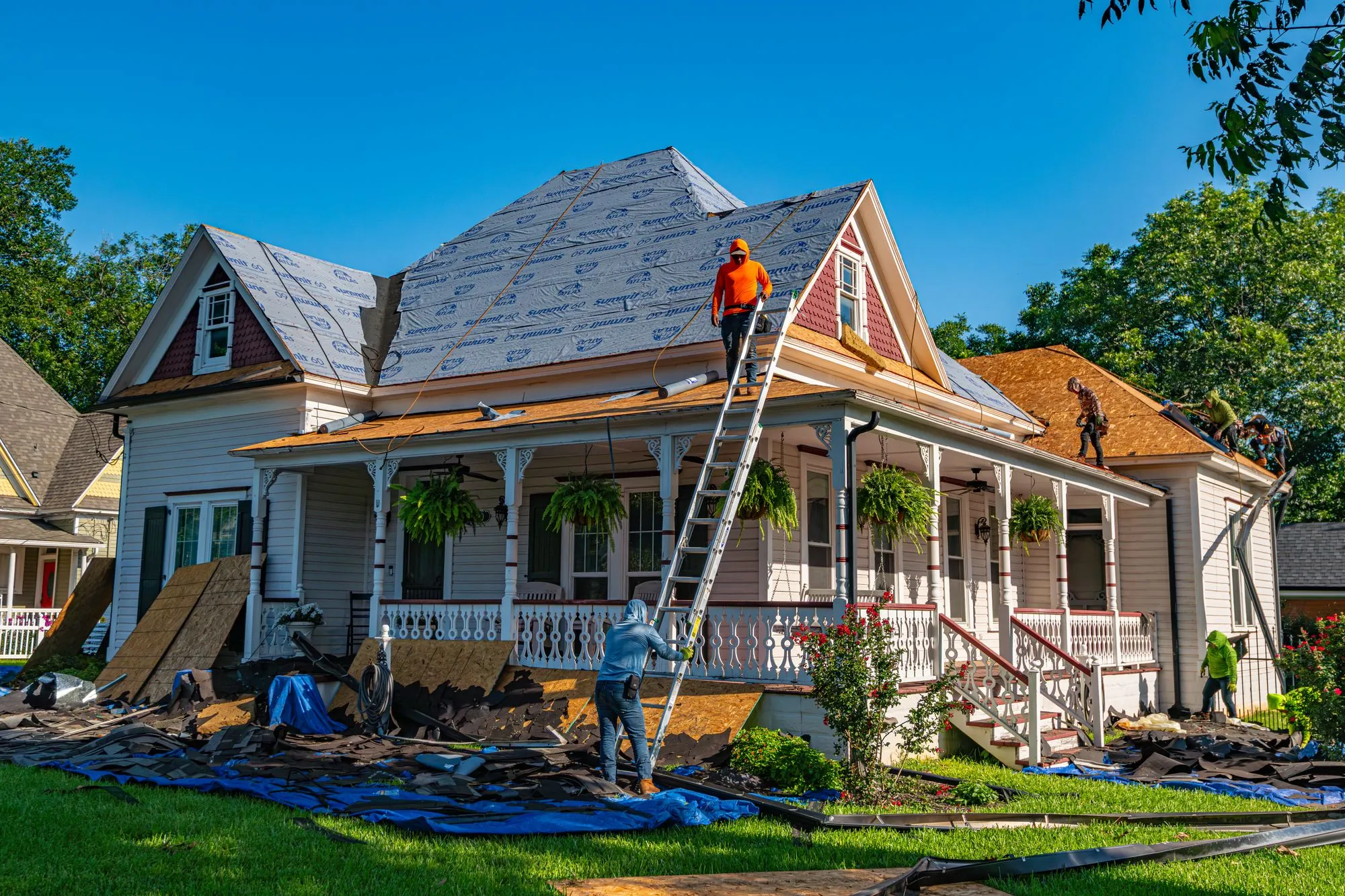 A crew re-roofing an older house, the covering stripped in sections