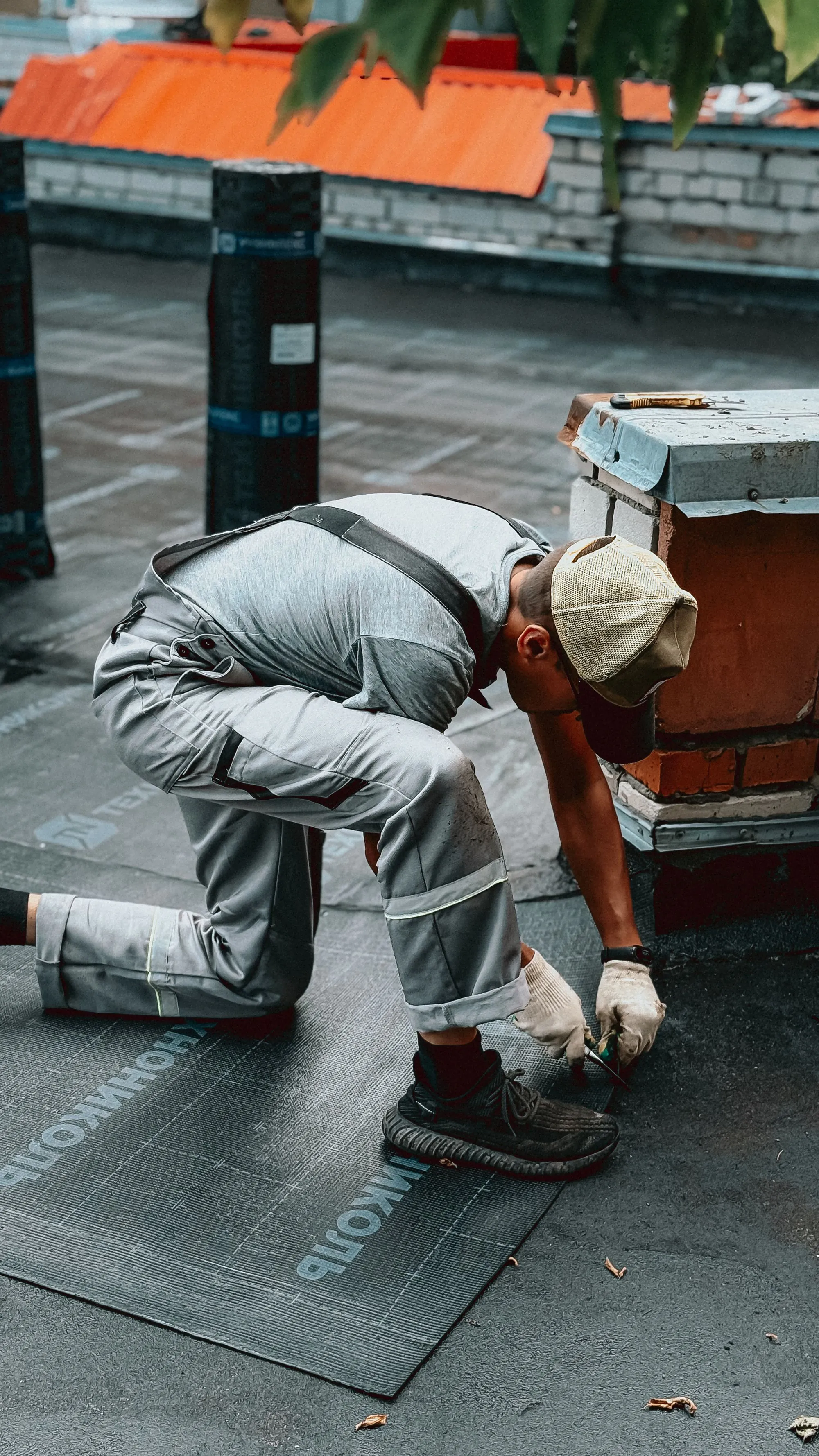 A roofer crouched over a repair beside a chimney stack