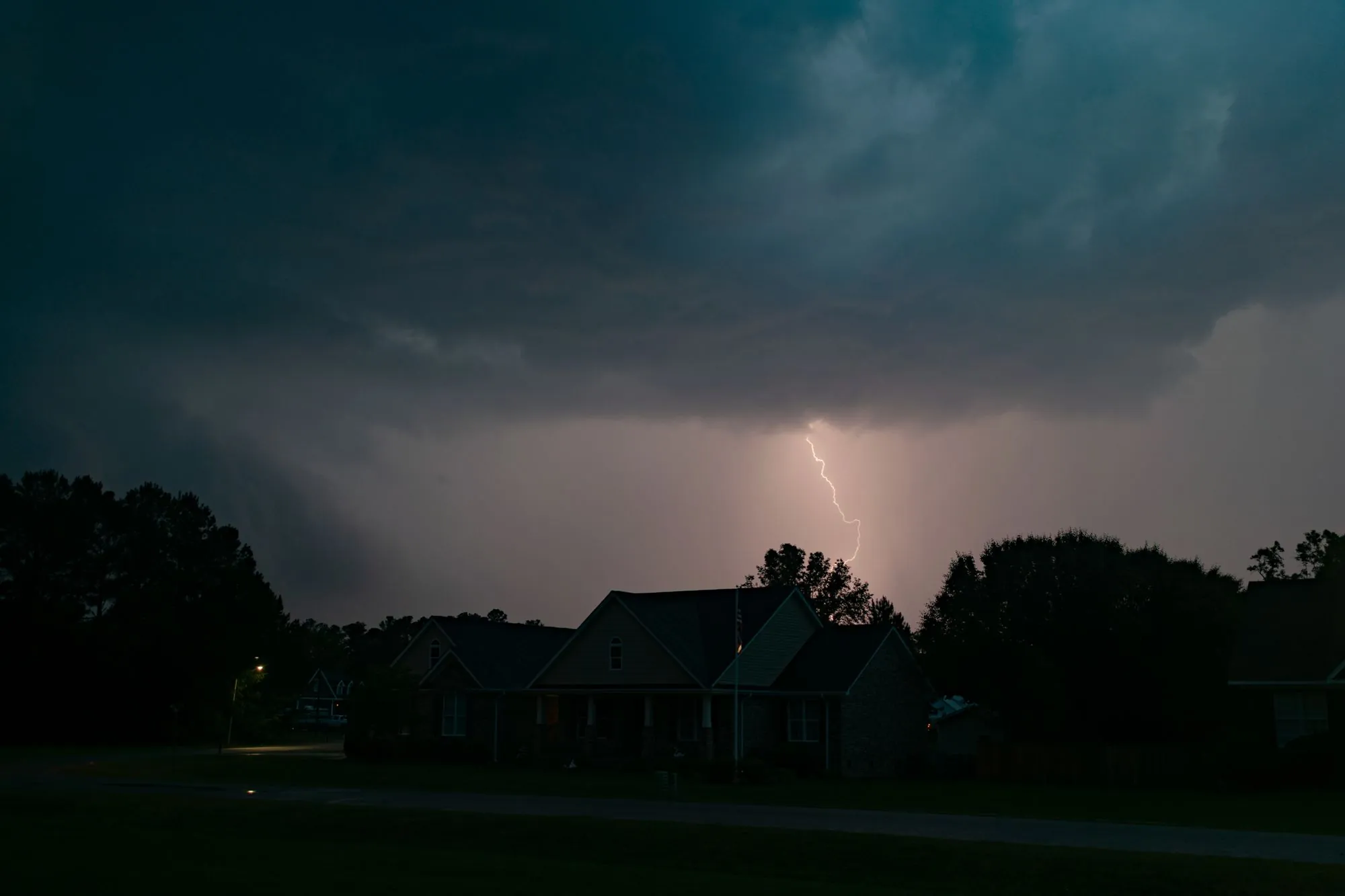Lightning breaking over houses under a dark evening sky